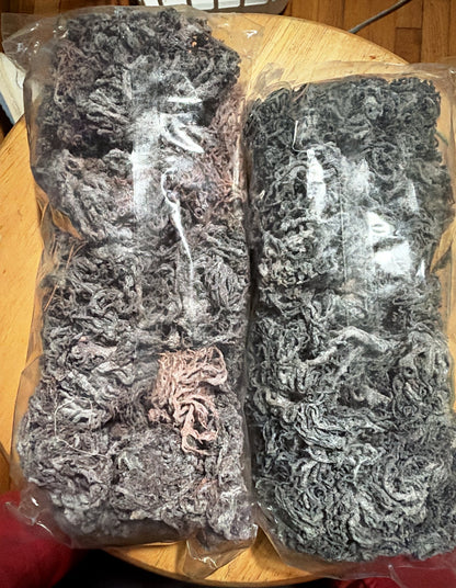 Back view of two bags of sun-dried Saint Lucian sea moss (one purple-label, one green-label; this photo doesn't show which is which) with the sea moss visible: dark purple-grey, with some natural pink strands.